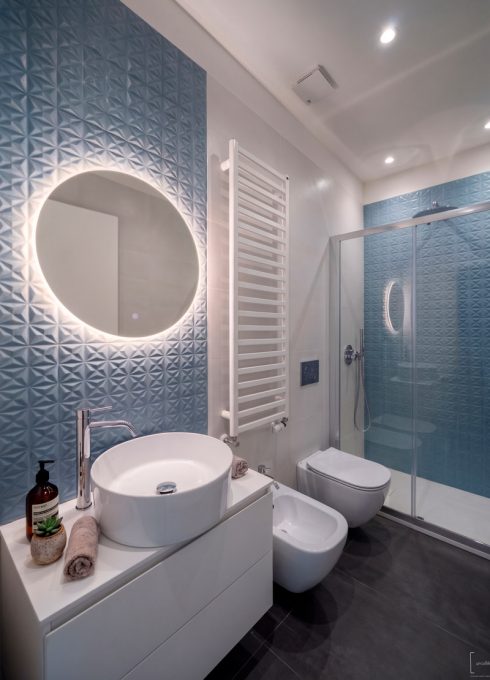 Bagno contemporaneo con rivestimento 3D azzurro e specchio retroilluminato