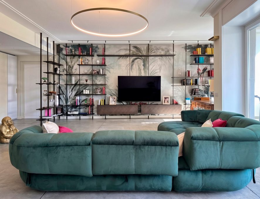 Zona living contemporanea con libreria modulare e divano verde petrolio in via Fetonte